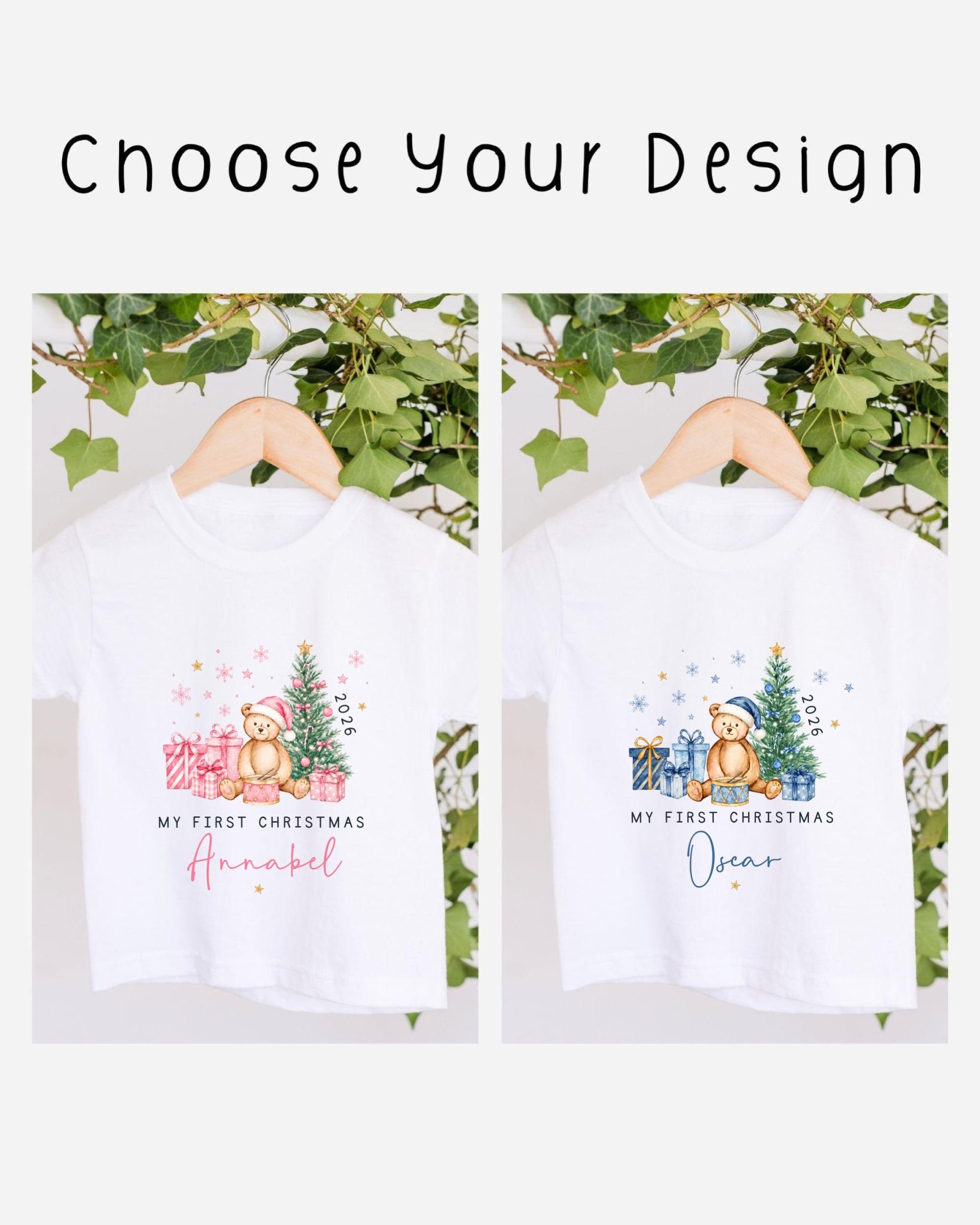 two white t-shirts with Christmas-themed designs, hanging on a wooden hanger. The t-shirts feature illustrations of a bear, a Christmas tree, and presents, along with the text "My first Christmas" and "My first Christmas" written on them.