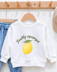 A white sweatshirt with a graphic of a lemon and the text "Freshly squeezed" printed on it, hanging on a wooden hanger.