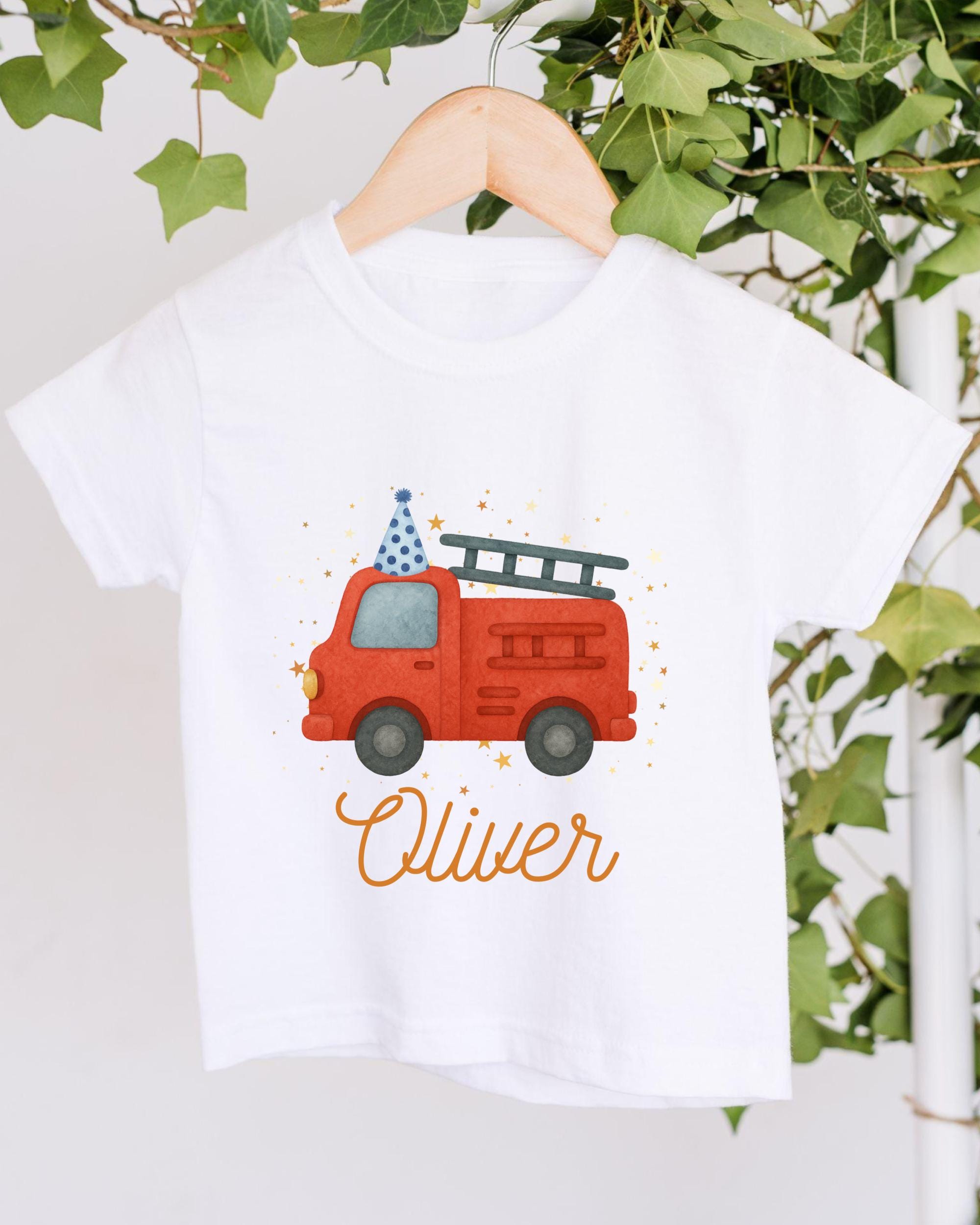 A white t-shirt with a red fire truck and a blue party hat printed on it, along with the name "Olivier" written below the image.