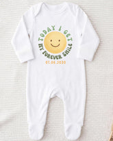 A white onesie with a smiley face and text printed on it.