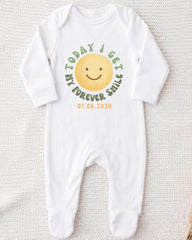 A white onesie with a smiley face and text printed on it.