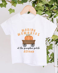 A white t-shirt with a graphic design featuring a pumpkin and a wagon, along with the text "Making memories at the pumpkin patch Alison".