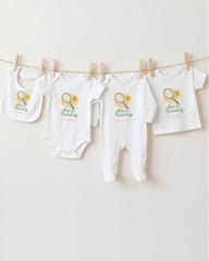 A row of white baby clothes with tennis-themed designs hanging on a clothesline.