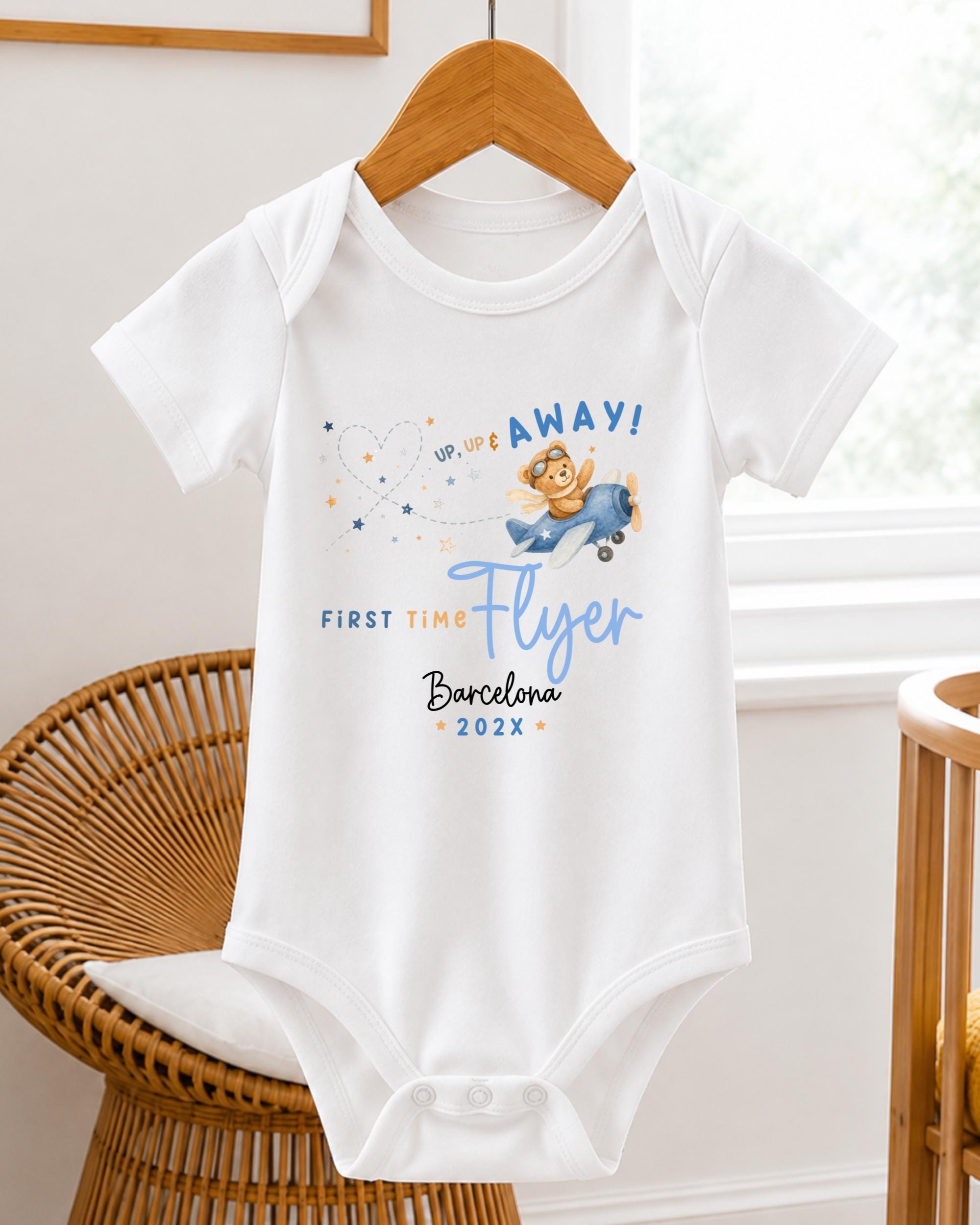 A white baby onesie with a graphic of a flying bear and text that says "UP TO YOUR AFFAY! FIRST TIME FLYER Barcelona 20XX".