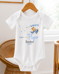 A white baby onesie with a graphic of a flying bear and text that says "UP TO YOUR AFFAY! FIRST TIME FLYER Barcelona 20XX".