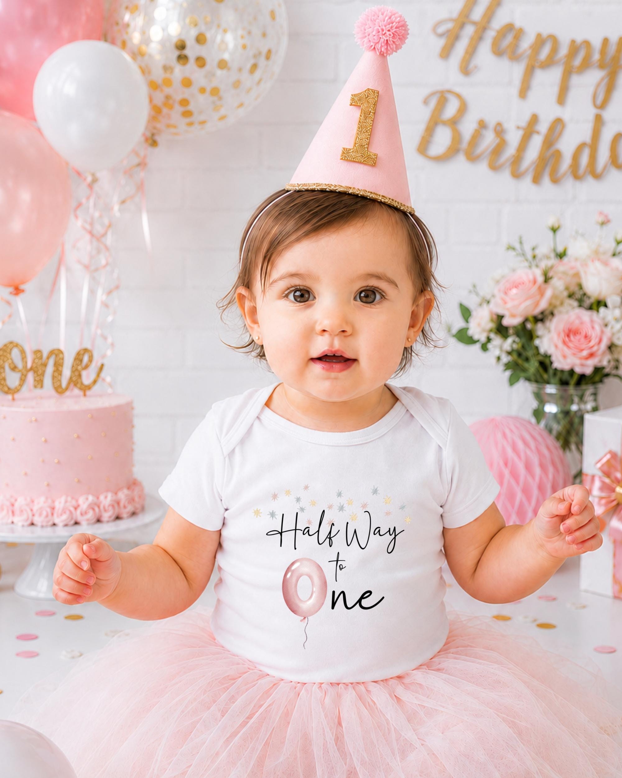 A young girl wearing a birthday hat and a white t-shirt with a birthday message is surrounded by balloons and a cake, celebrating her first birthday.