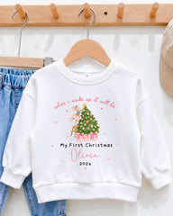 A white sweatshirt with a Christmas tree design and text printed on it, hanging on a wooden hanger.