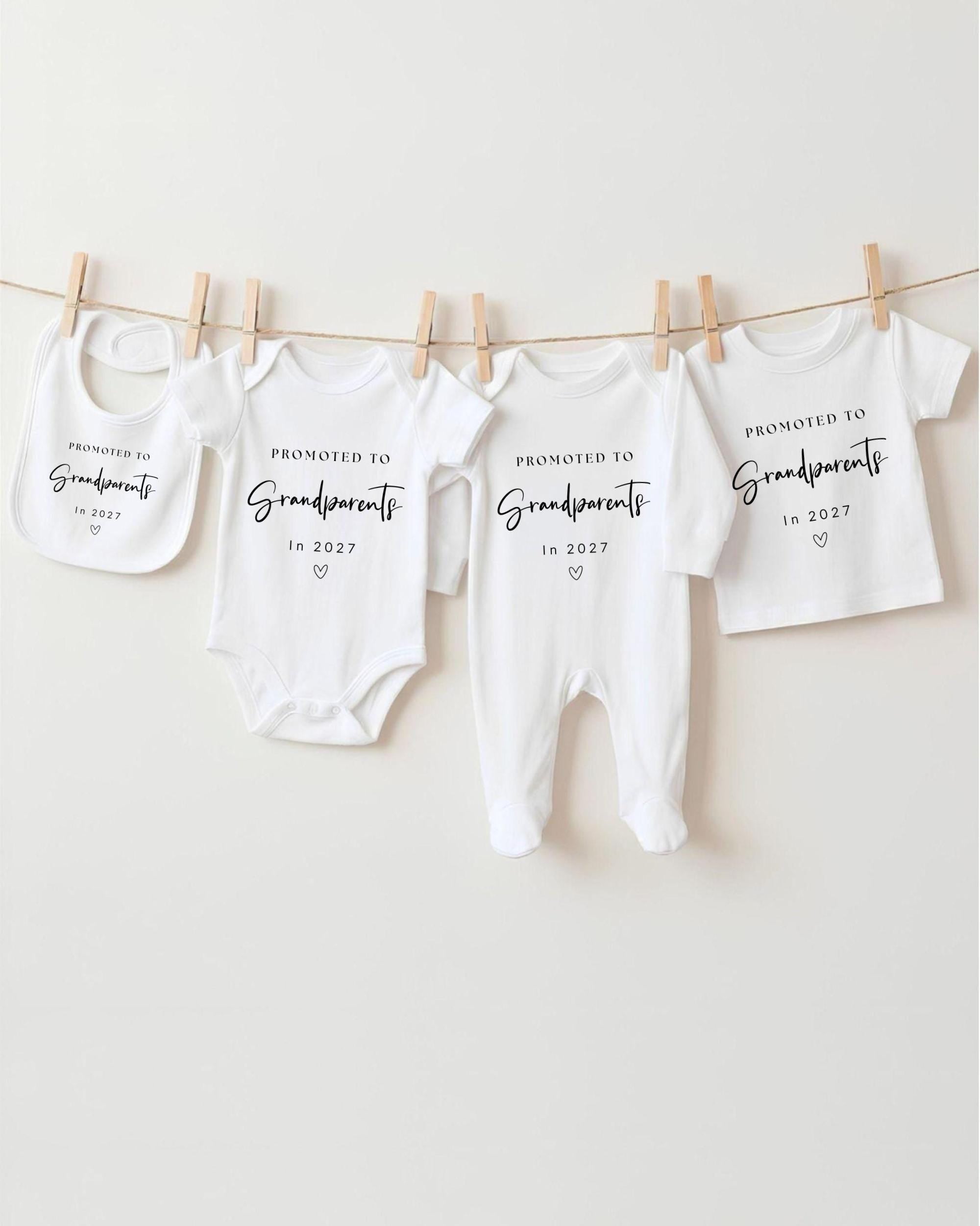 A row of white baby clothes with black text that reads "Promoted to Grandparents in 2027" hanging on a clothesline.