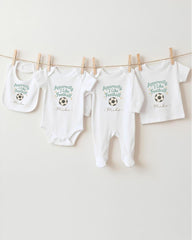 a collection of four white baby clothes hanging on a clothesline, each with a unique design and text printed on them.