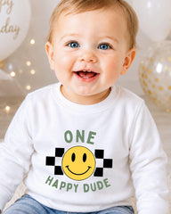 A smiling baby boy wearing a white shirt with a happy face and the text "ONE HAPPY DUDE" printed on it.
