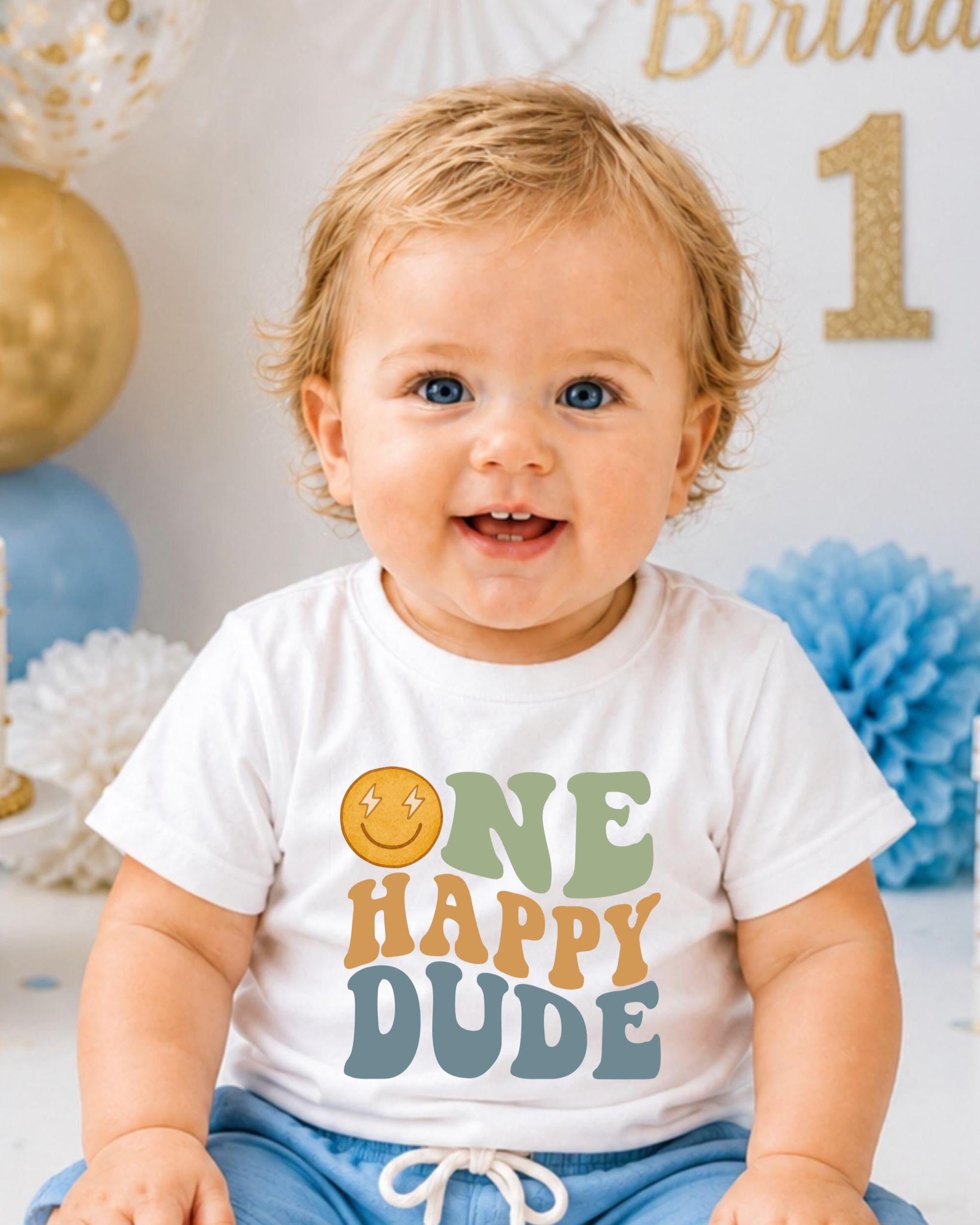A smiling baby boy wearing a white t-shirt with a happy face and the text "ONE HAPPY DUDE" printed on it.