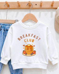 A white sweatshirt with the text "BREAKFAST CLUB" printed on it, along with an illustration of pancakes and fruit.