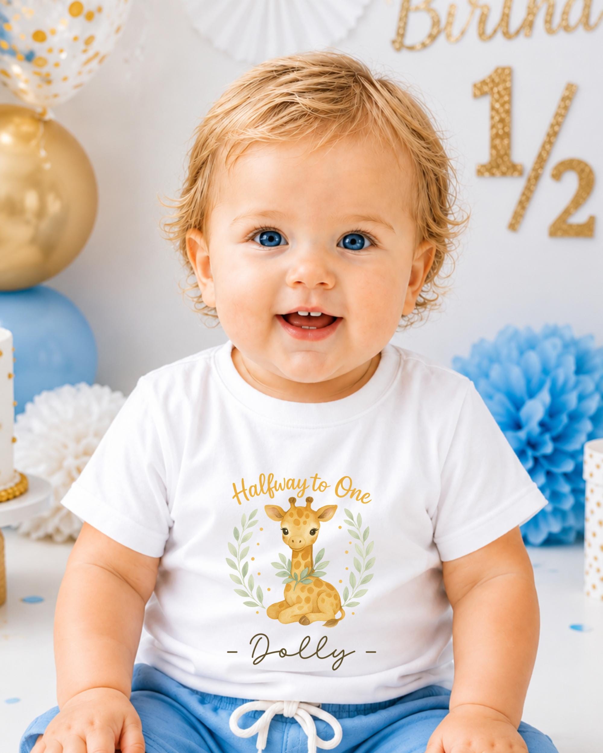 A smiling baby boy wearing a white t-shirt with a giraffe graphic and the text "Halfway to One - Dolly" is sitting in front of a birthday party backdrop with gold and blue decorations.
