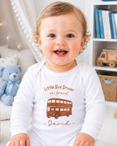 A smiling baby boy wearing a white onesie with a double-decker bus design and the text "Little Bus Driver on board David" printed on it.