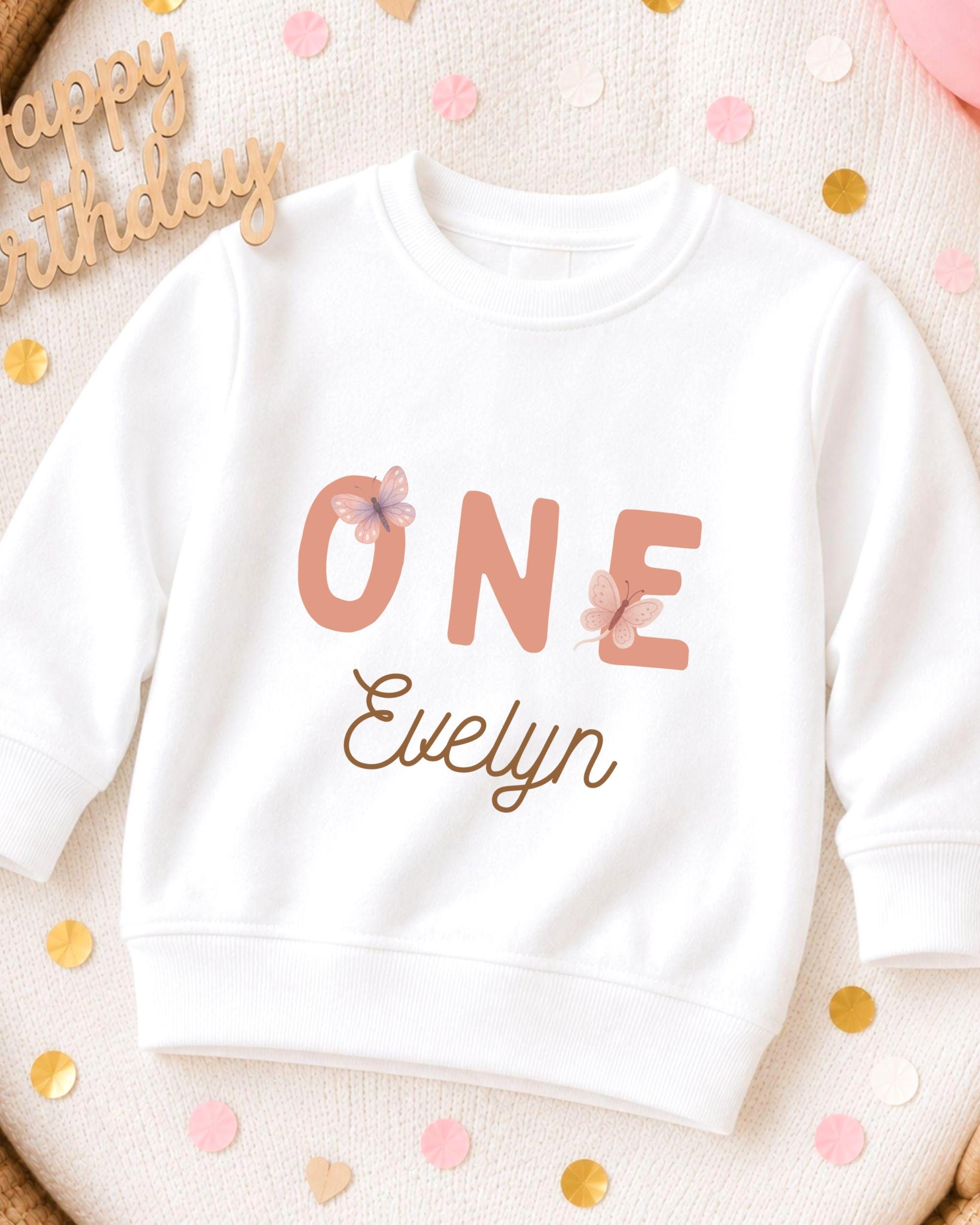 A white sweatshirt with the text "ONE Evelyn" printed on it, surrounded by confetti.
