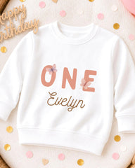 A white sweatshirt with the text "ONE Evelyn" printed on it, surrounded by confetti.