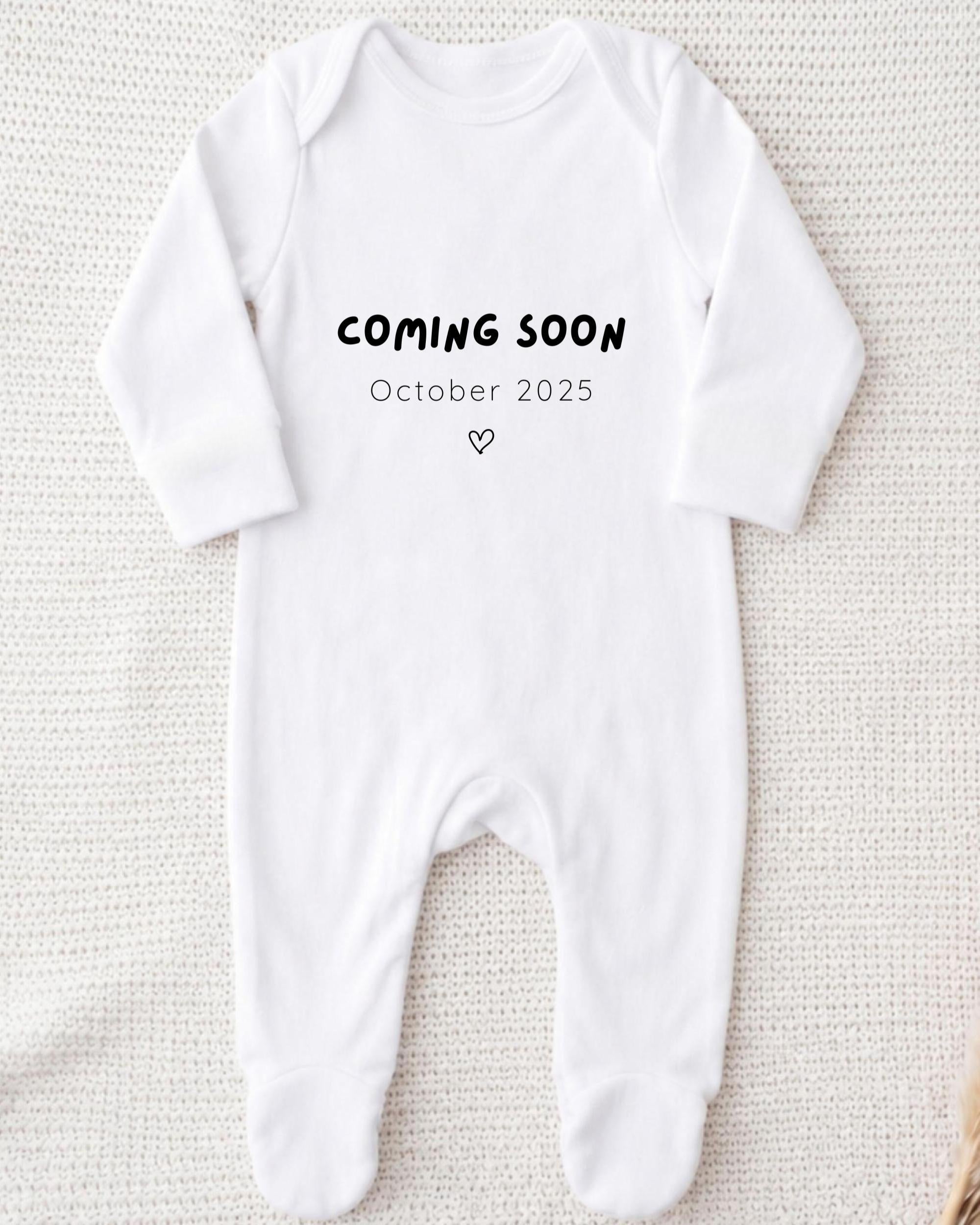 A white onesie with the text "COMING SOON October 2025" printed on it.