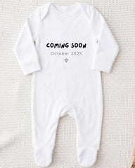 A white onesie with the text "COMING SOON October 2025" printed on it.