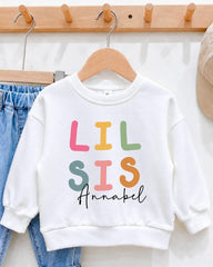 A white sweatshirt with colorful text printed on it, hanging on a wooden hanger.