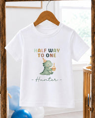 A white t-shirt with a cartoon dinosaur wearing a party hat and holding a birthday cake, along with the text "Half Way to One Hunter" printed on it.