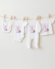 A collection of white baby clothes, including onesies and pajamas, with the name 'Emma' printed on them, along with a mermaid image. The clothes are hanging on a clothesline.