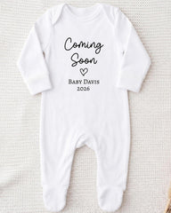 A white onesie with the text "Coming Soon Baby Davis 2026" printed on it.