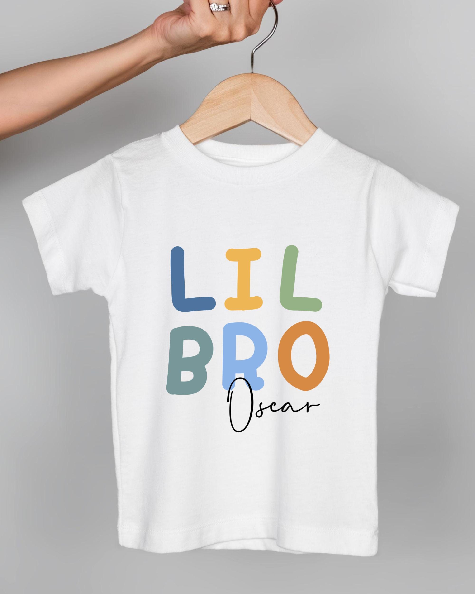 A person's hand is holding a white t-shirt with the text "LIL BRO Oscar" printed on it.