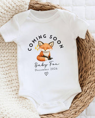 A white baby onesie with a graphic of a fox and the text "Coming soon Baby Fox December 2026" printed on it.