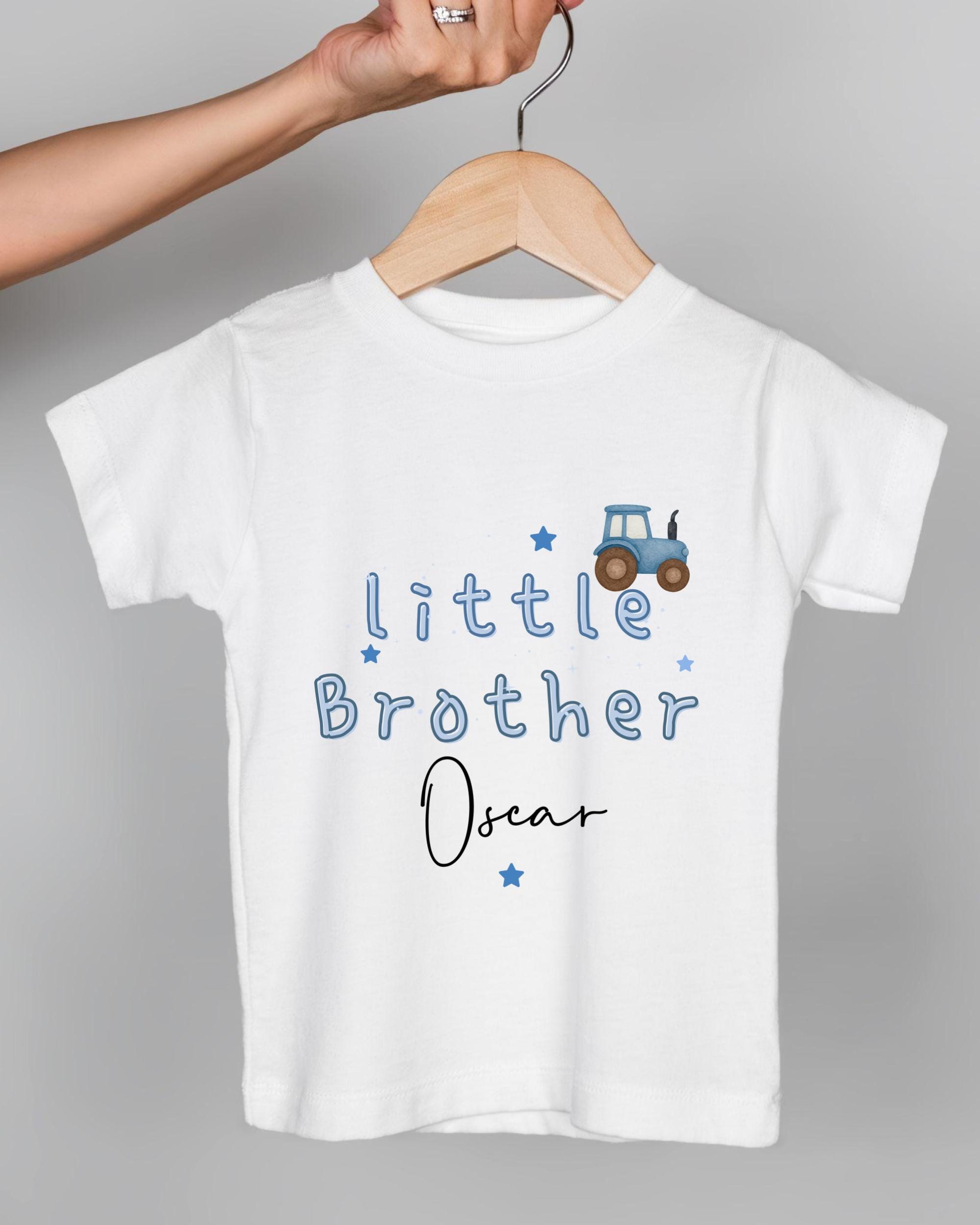 A white t-shirt with blue text and a tractor graphic, hanging on a wooden hanger.