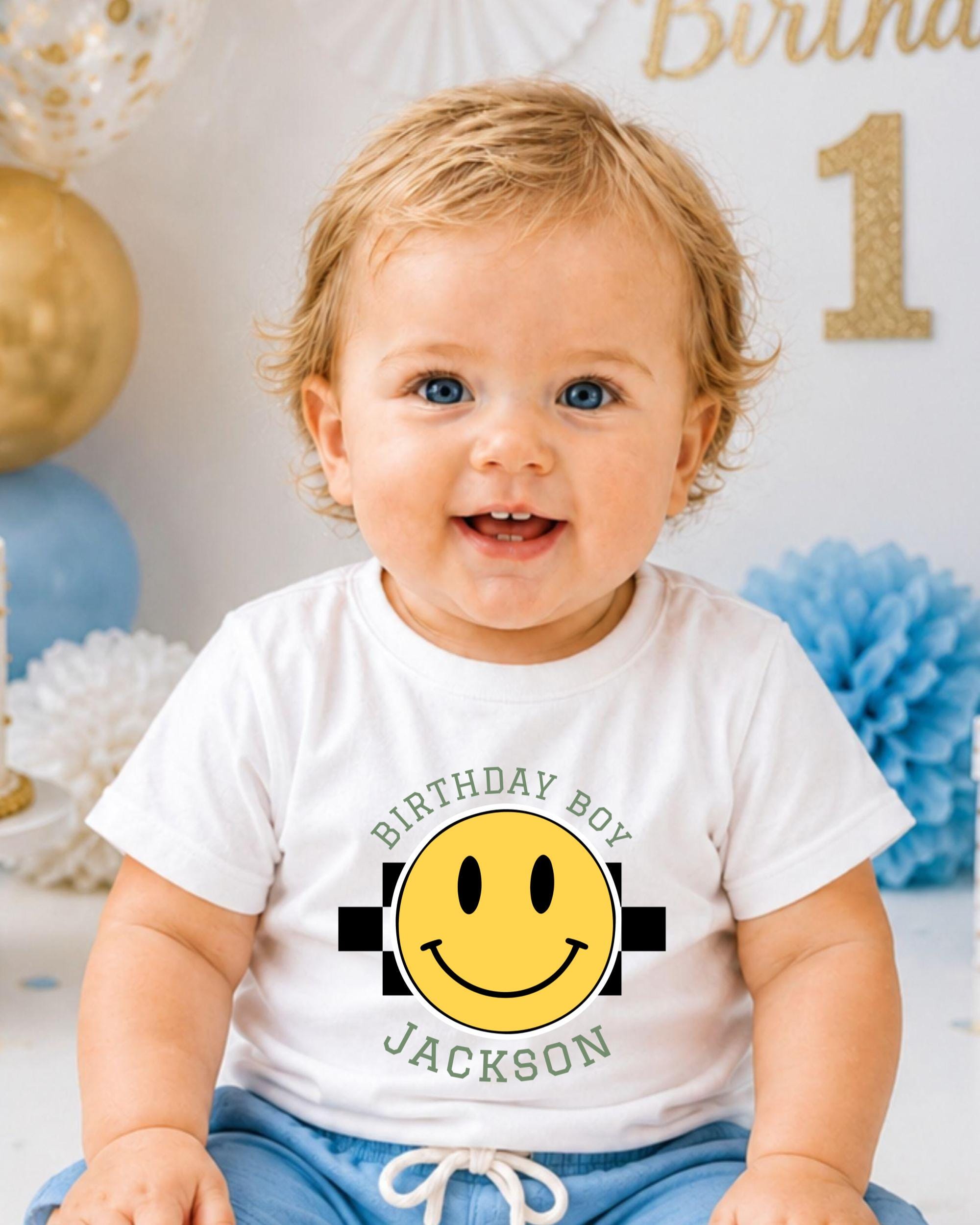 A smiling baby boy wearing a white t-shirt with a yellow smiley face and text that says "Birthday Boy Jackson".