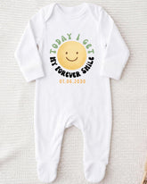 A white onesie with a smiley face design and text printed on it.