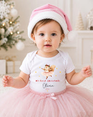 A young girl wearing a pink Santa hat and a white t-shirt with a cartoon character on it, posing in front of a Christmas tree.