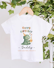 A white t-shirt with a graphic design of a dinosaur wearing a birthday hat and holding a cupcake, along with the text "Happy Birthday Daddy - Love you lots, Oscar x".