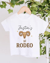 A white t-shirt with a graphic design and text printed on it, hanging on a wooden hanger.