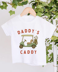 A white t-shirt with a graphic design of a golf cart and the text "DADDY'S CADDY" printed on it.