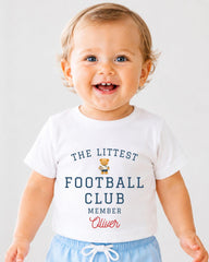 A smiling baby boy wearing a white t-shirt with text and a small teddy bear graphic.