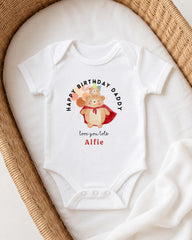 A white onesie with a graphic of a bear and the text "Happy Birthday Daddy" printed on it, placed on a white blanket.