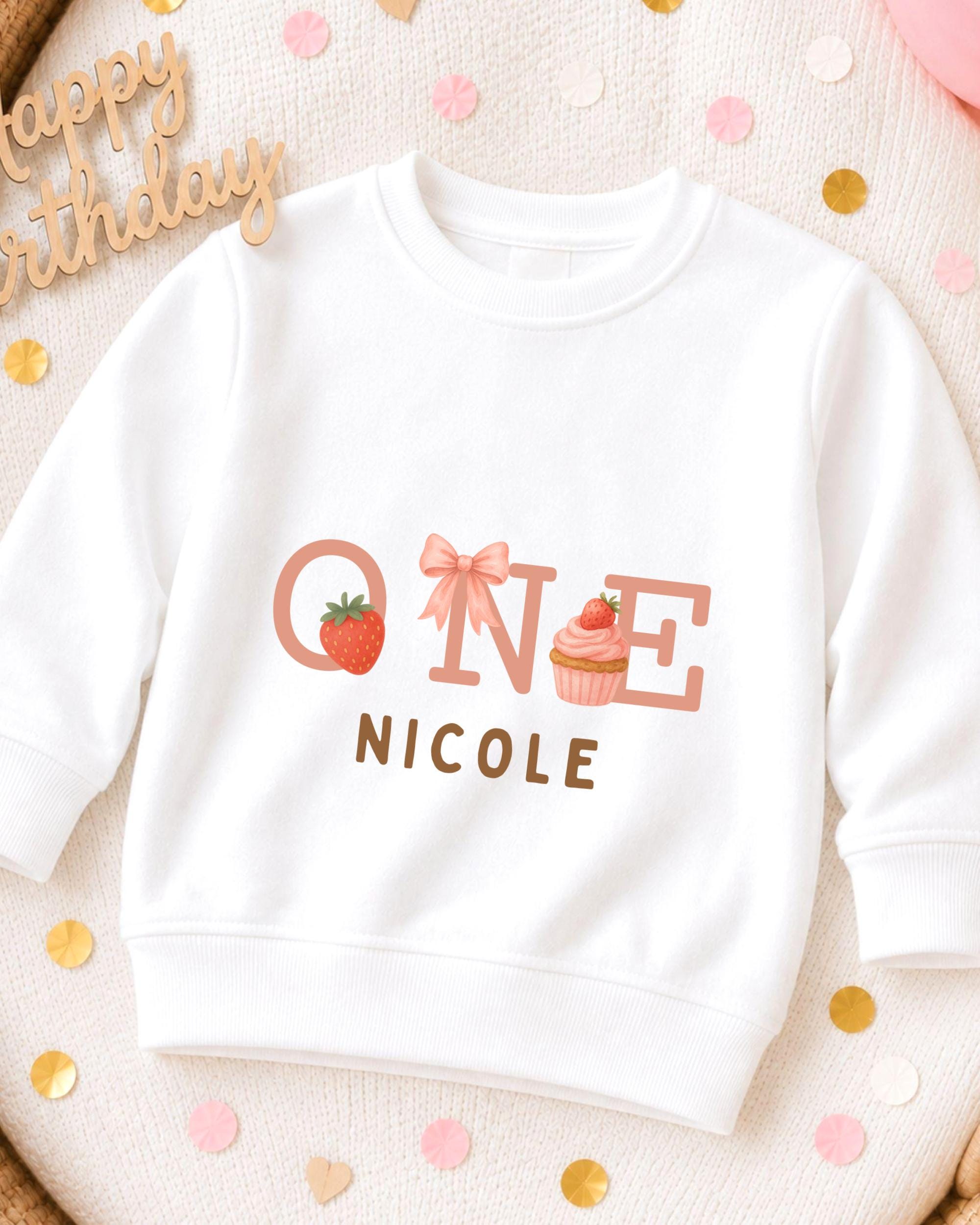 A white sweatshirt with a personalized text and graphics design, including a strawberry, cupcake, and the text "ONE NICOLE".