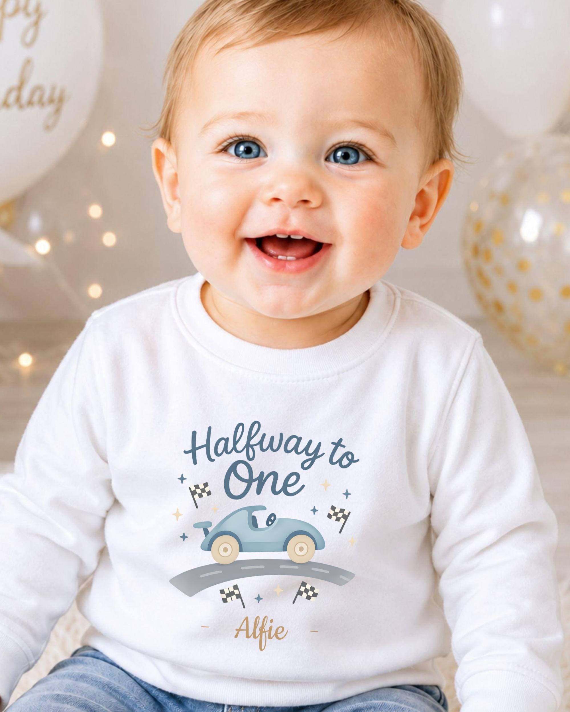 A smiling baby boy wearing a white shirt with a graphic of a car and the text "Halfway to One" and "Alfie" printed on it.