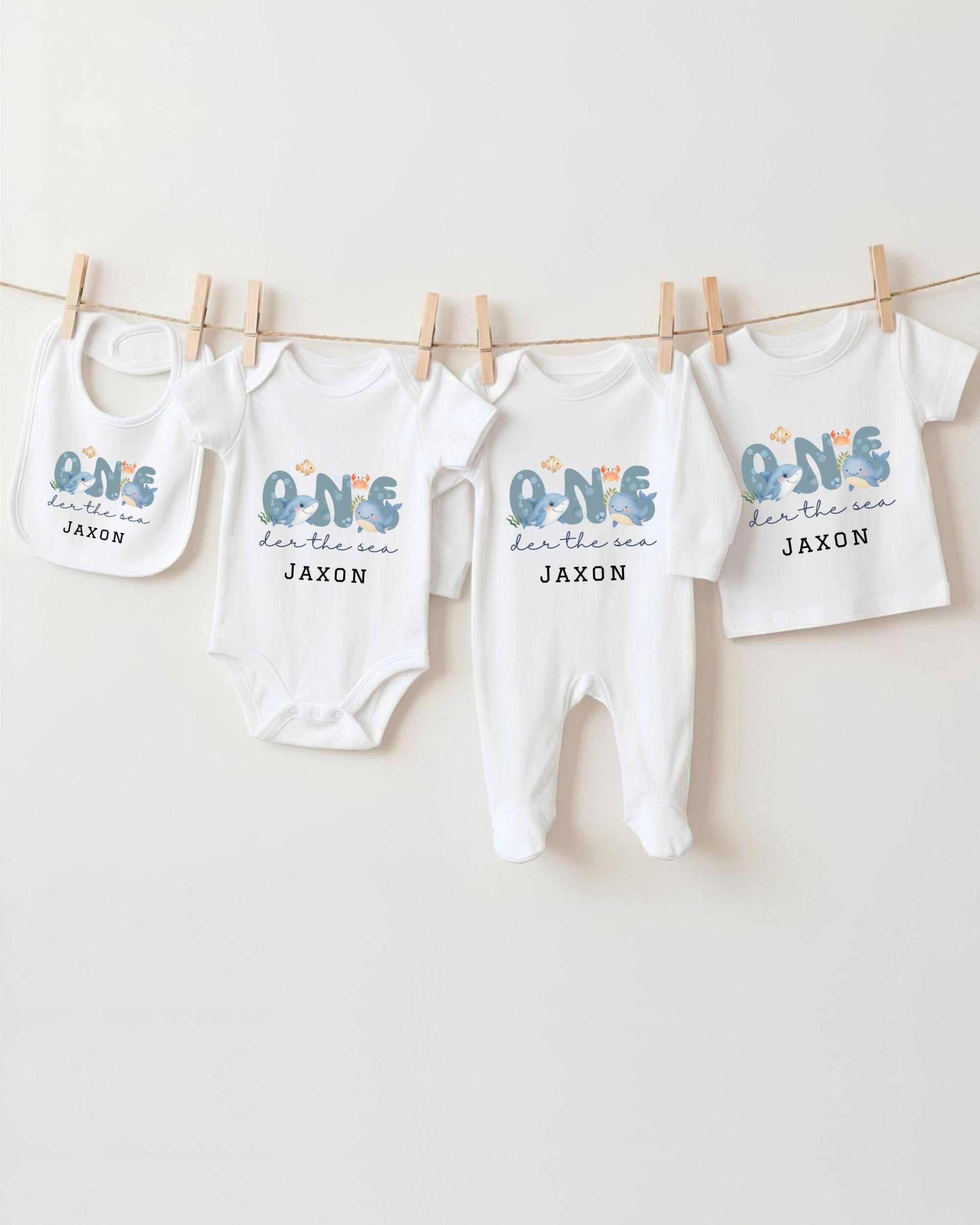 A collection of four white baby clothes, including onesies and pajamas, hanging on a clothesline.