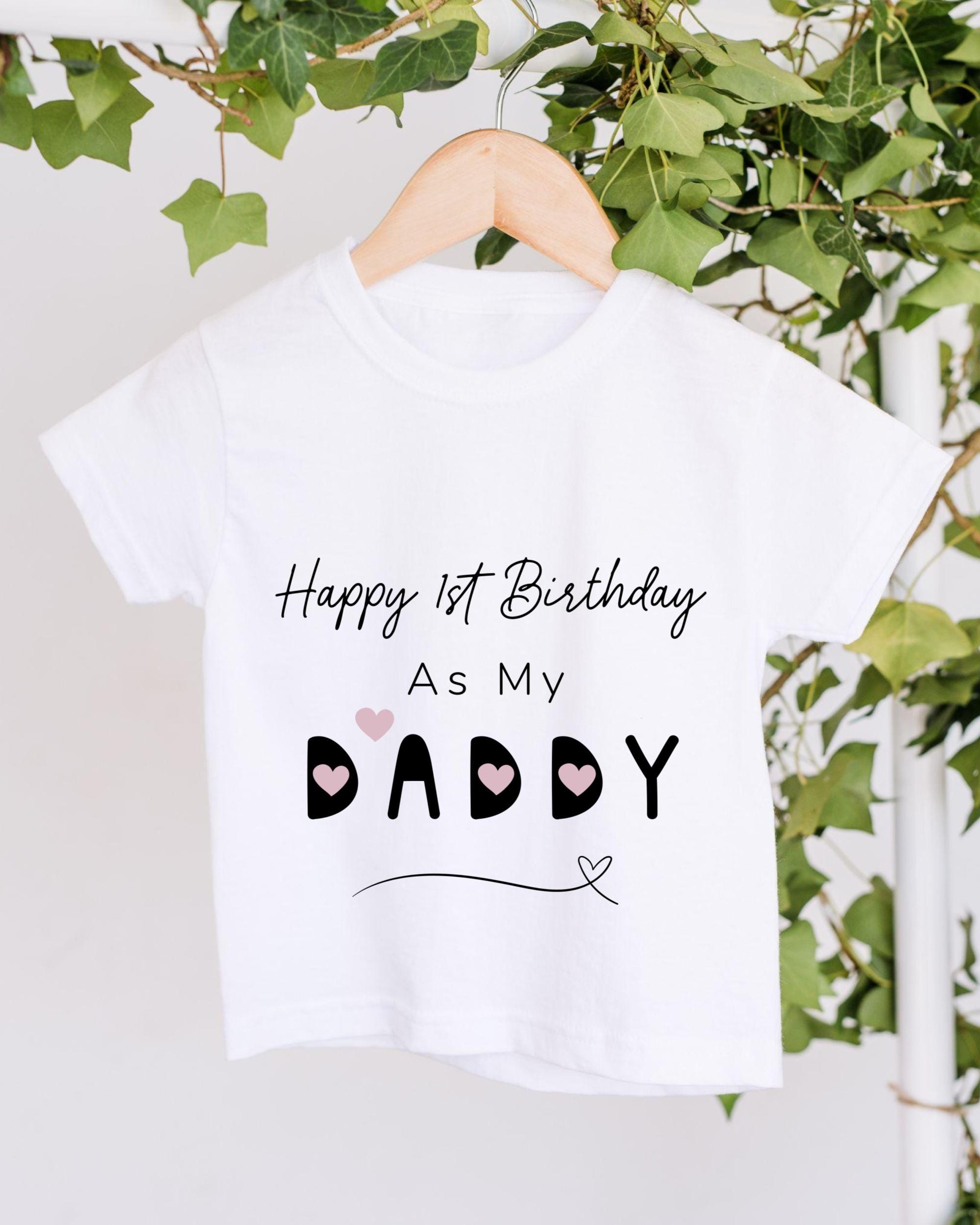 A white t-shirt with text and graphics hanging on a wooden hanger, with greenery in the background.