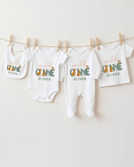 A collection of baby clothes and bibs hanging on a clothesline, with the clothes featuring the name "OLIVER" printed on them.