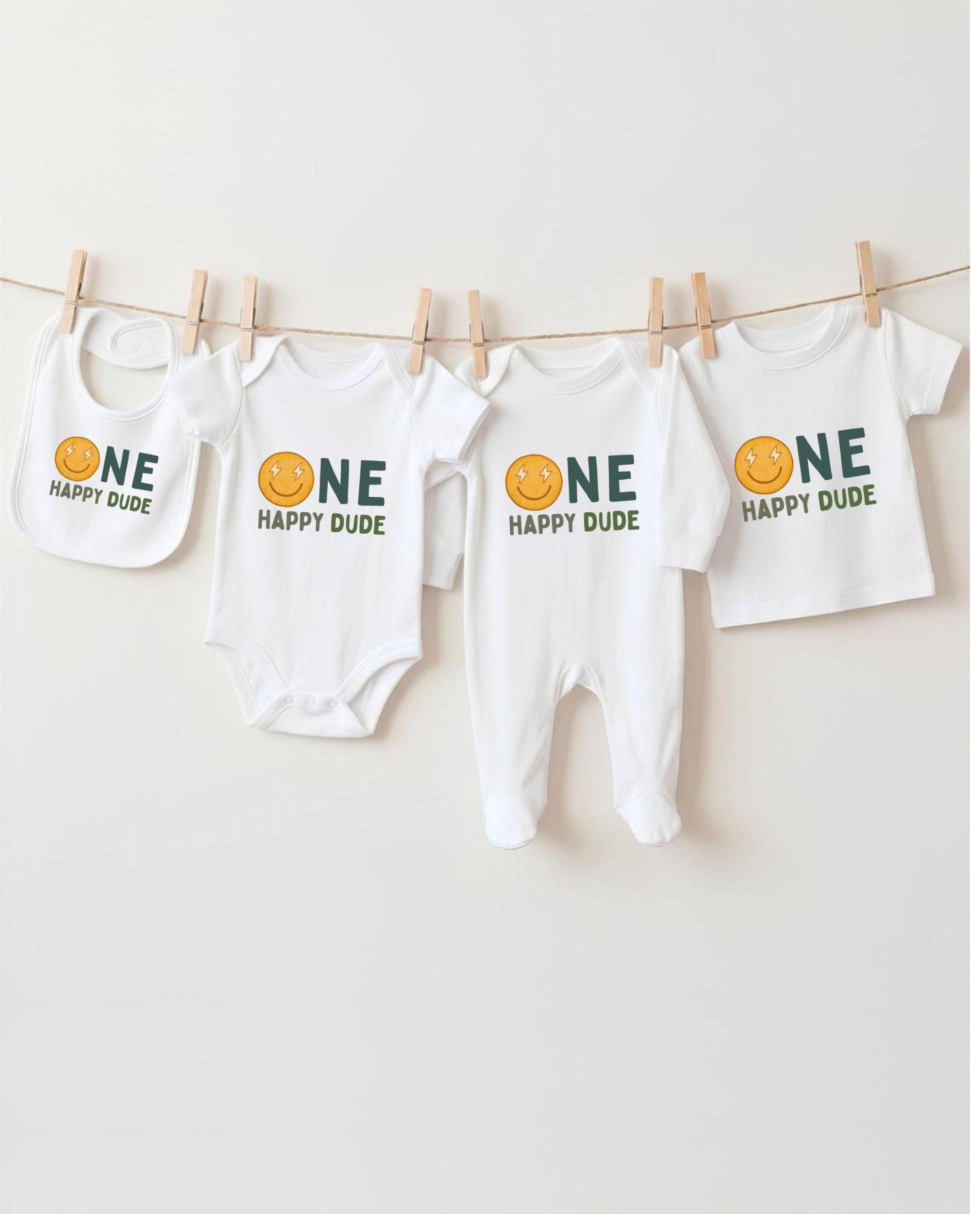 A collection of four white baby clothes with the text "ONE HAPPY DUDE" printed on them, hanging on a clothesline.