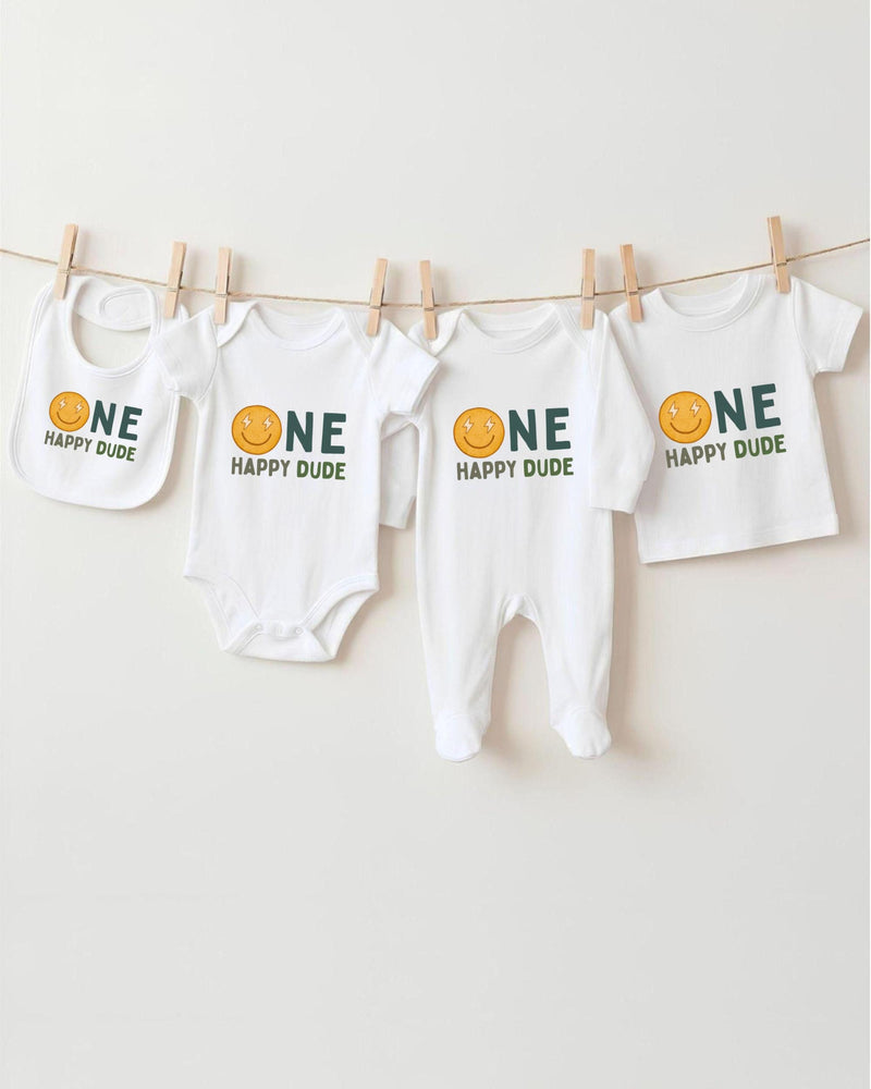 A collection of four white baby clothes with the text "ONE HAPPY DUDE" printed on them, hanging on a clothesline.