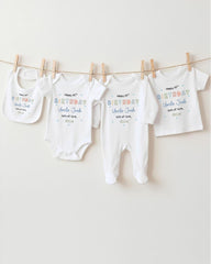 A row of four white baby clothes, including onesies and bibs, hanging on a clothesline.