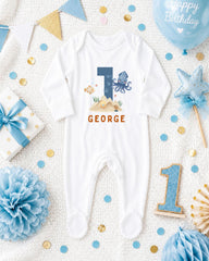 A white onesie with the number 1 and an octopus design, surrounded by birthday decorations such as a blue balloon, blue and gold confetti, and a blue and gold star.