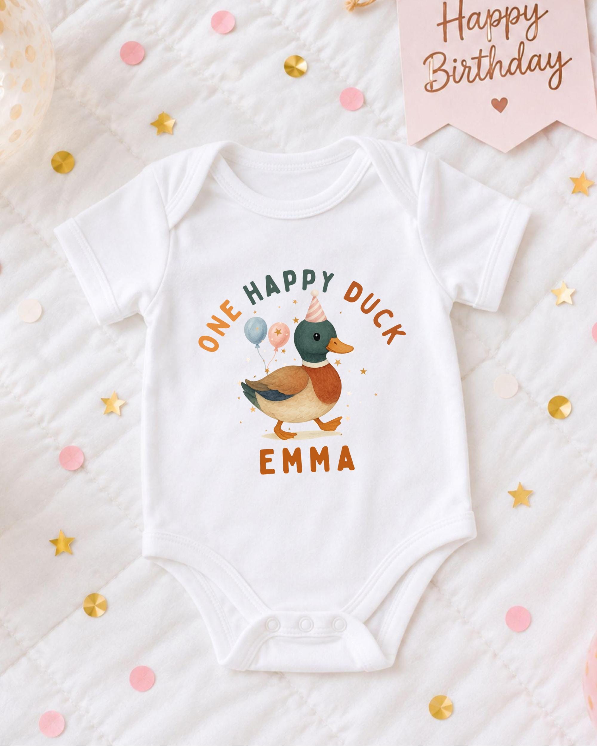 A white onesie with a cartoon duck and the text "One Happy Duck Emma" printed on it, surrounded by confetti and a birthday card.