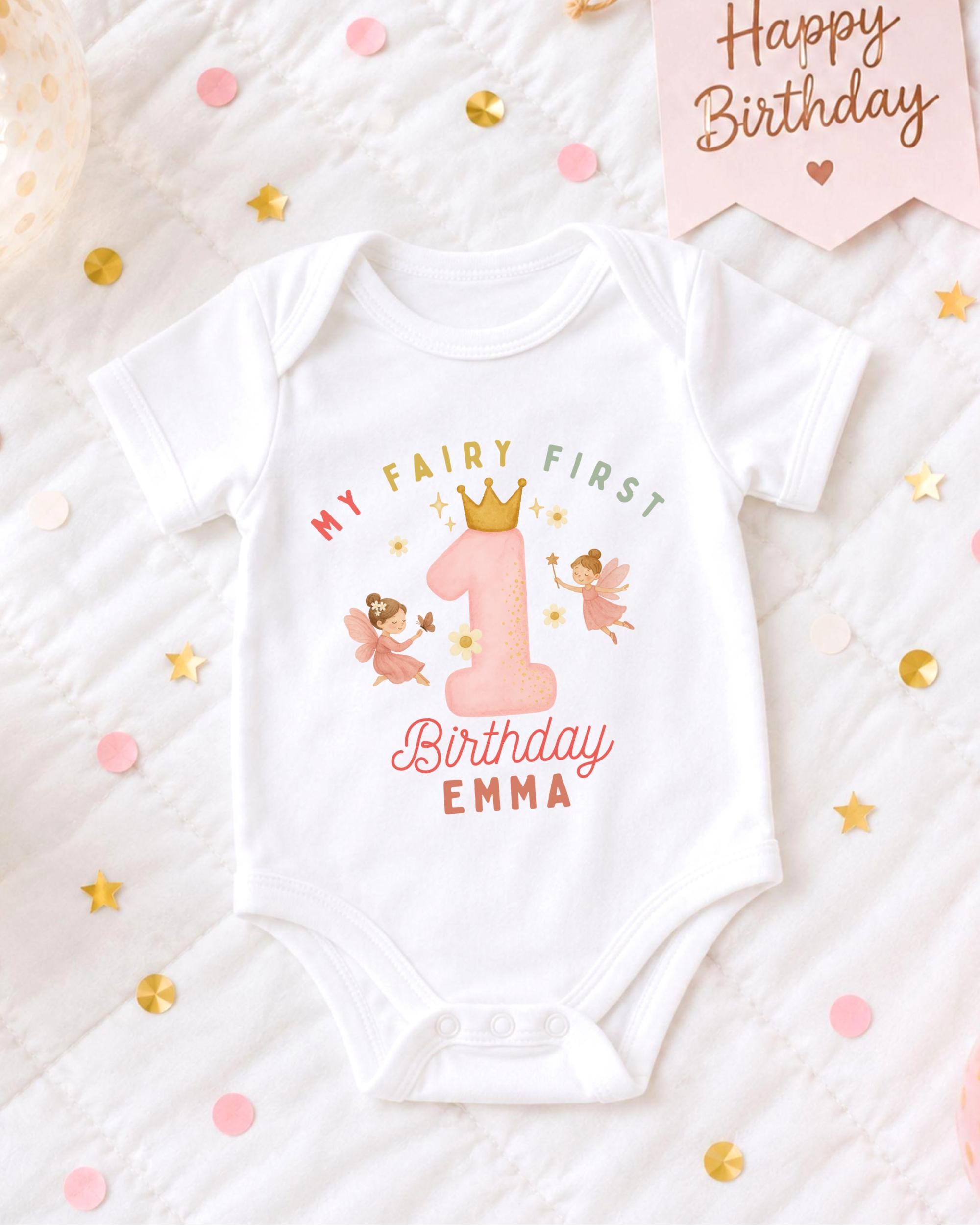 A white onesie with a birthday message and a fairy design, surrounded by confetti and a birthday card.