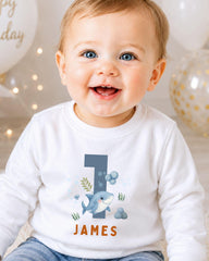 A smiling baby boy wearing a white shirt with a shark graphic and the name "James" printed on it.