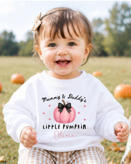 A smiling baby girl wearing a white sweater with a pumpkin design and text that says "Mummy & Daddy's Little Pumpkin Olivia".